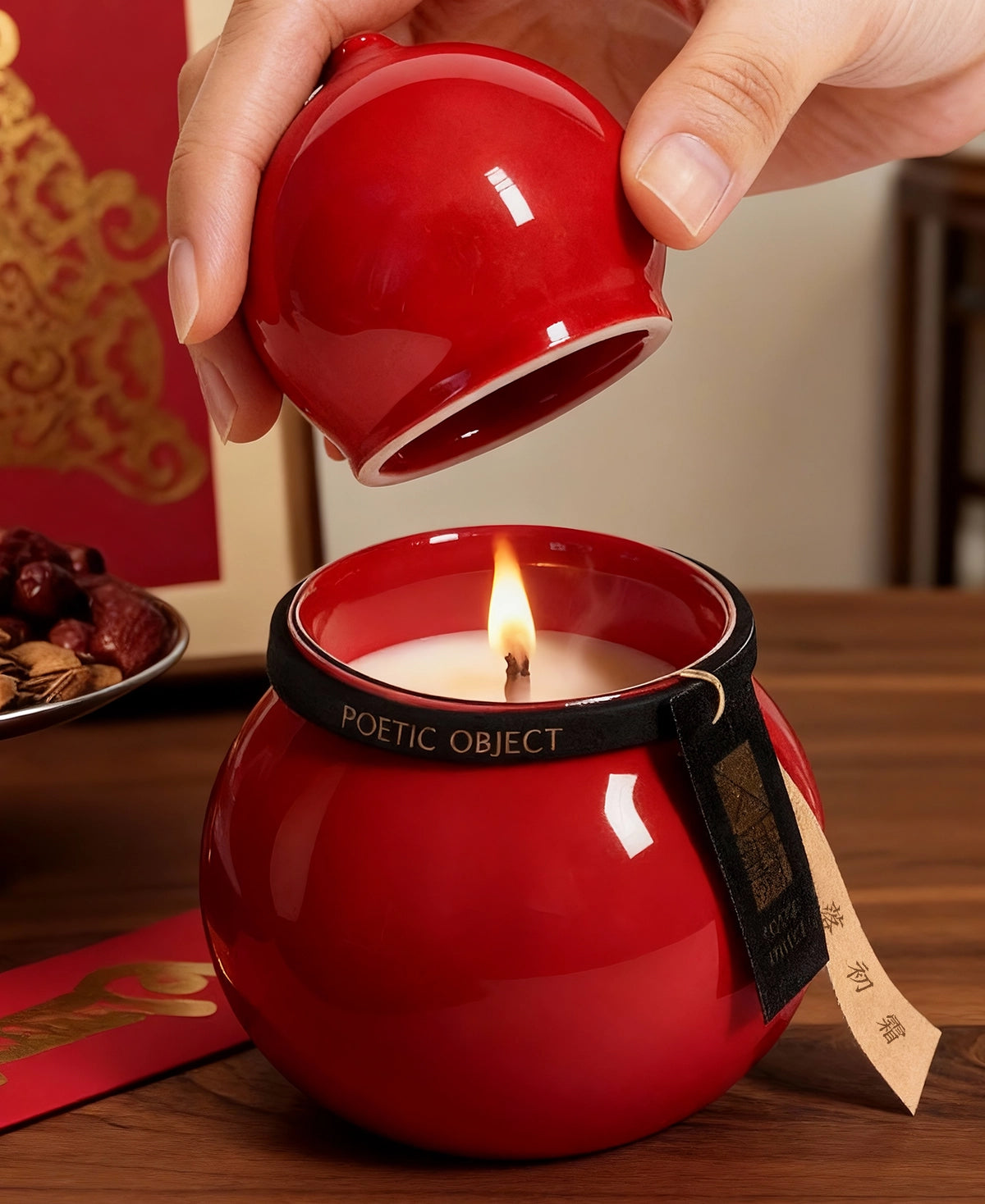 A hand lifting the lid of a lit red porcelain aromatic candle, creating a warm and lucky ambiance for home meditation.