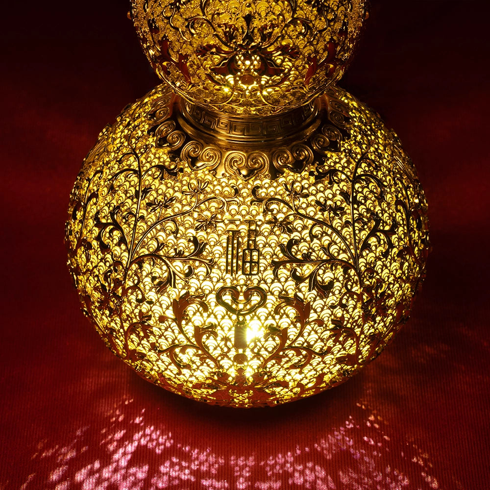 Gold filigree gourd art piece illuminated in the dark, casting mesmerizing shadows through its intricate hollow brass pattern.