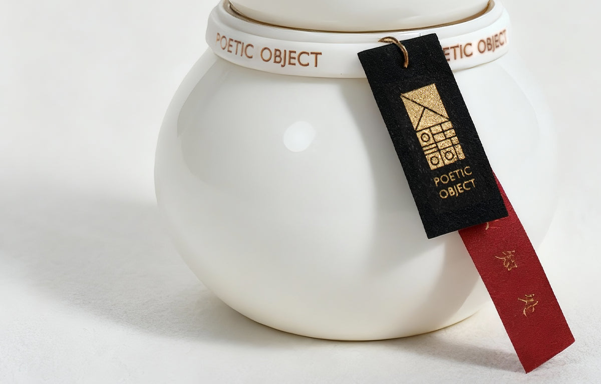 Detail of pure Dehua white porcelain candle body with decorative black and red tag, featuring an elegant organic curved silhouette.