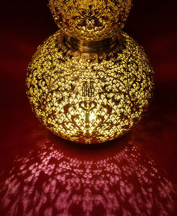 Illuminated gold hollow-out sculpture casting artistic shadows on a red surface, creating a warm and mysterious ambiance.