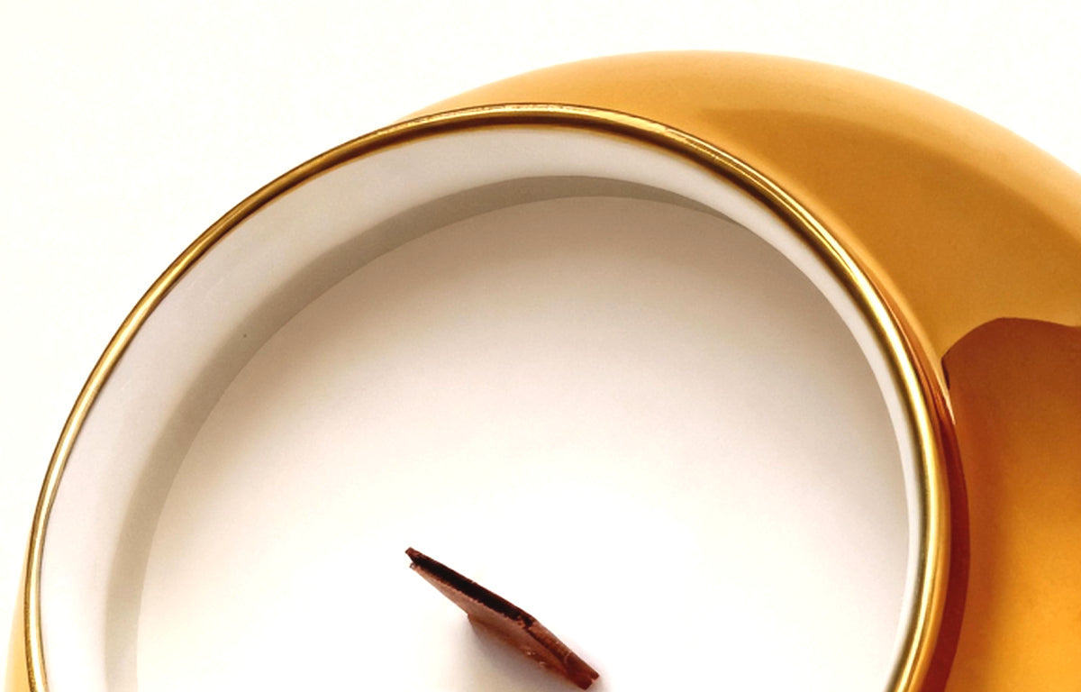 Macro view of the gold-plated rim and natural wood wick of an artisanal porcelain candle, showcasing premium soy wax quality.